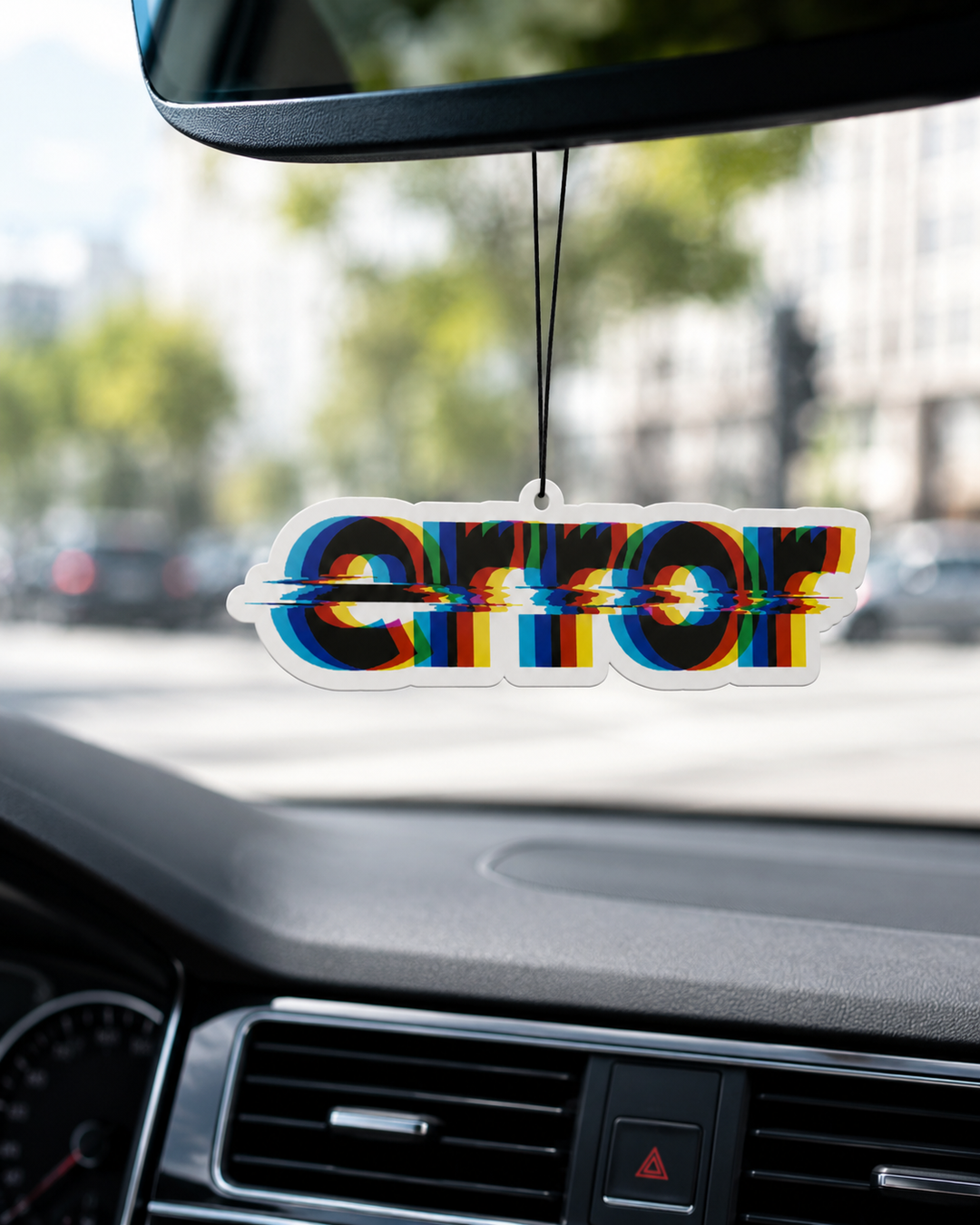 A car air freshener featuring the word 'ERROR' in a 3D anaglyph style with red, blue, and green chromatic aberration effects, hanging from a rearview mirror inside a car.