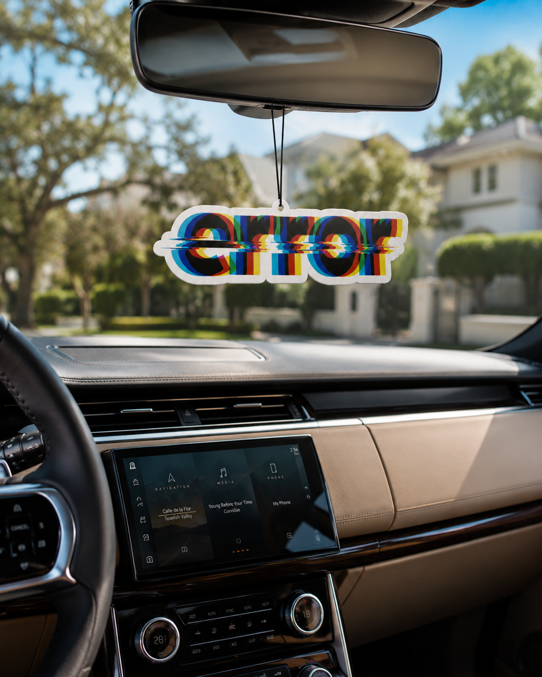 A die-cut car air freshener with the word 'ERROR' in a 3D glitch-style font, hanging from a rearview mirror inside a car cabin with a blurred suburban street background.
