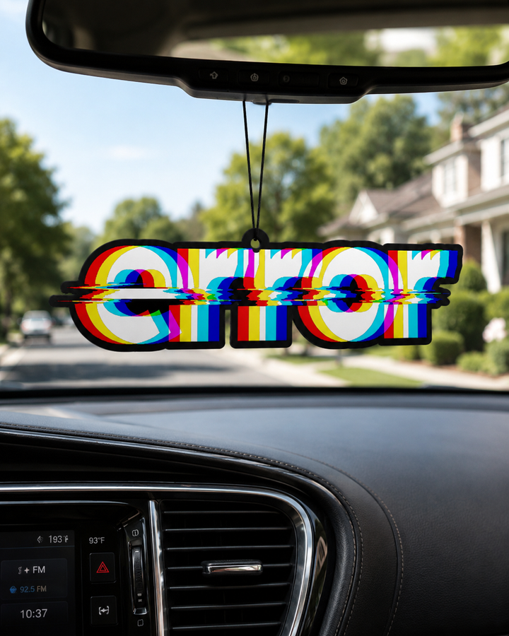 A colorful car air freshener spelling 'ERROR' hangs from the rearview mirror inside a car, with a blurred suburban street and houses visible through the windshield.